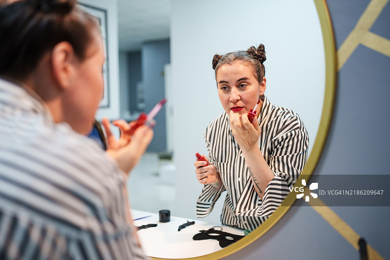 双丸子头的女性在镜子前涂口红。图片素材