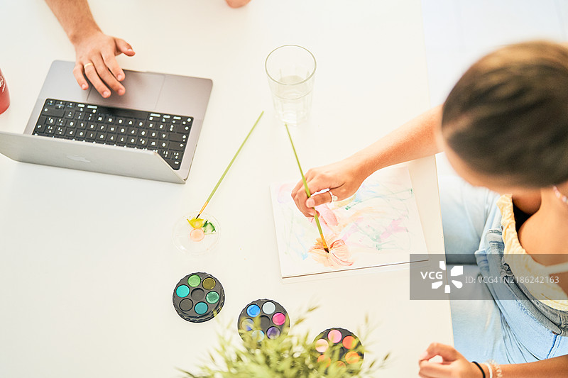 年轻艺术家在家中的办公桌上用水彩画画图片素材