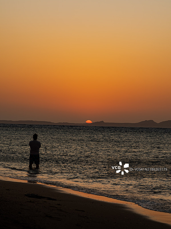 背影的男人站在海滩上，背景是橙色的天空，南西奈，埃及图片素材