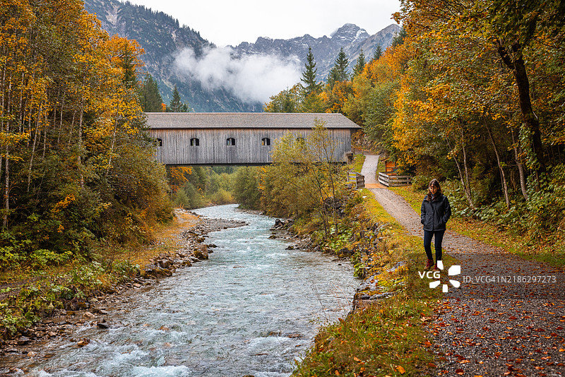 女性游客在奥地利阿尔卑斯山探索一条野生山河和一座有顶桥。图片素材