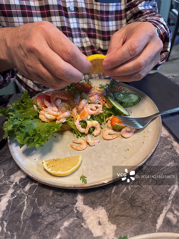 他正在把柠檬汁挤在虾上。图片素材