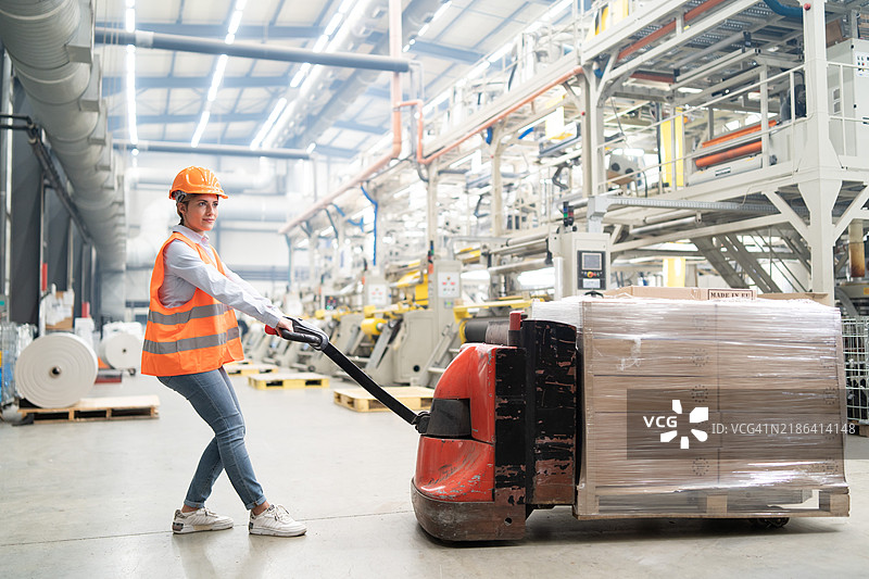 穿着安全装备的仓库工人操作托盘车，展现了供应链任务中的高效。图片素材
