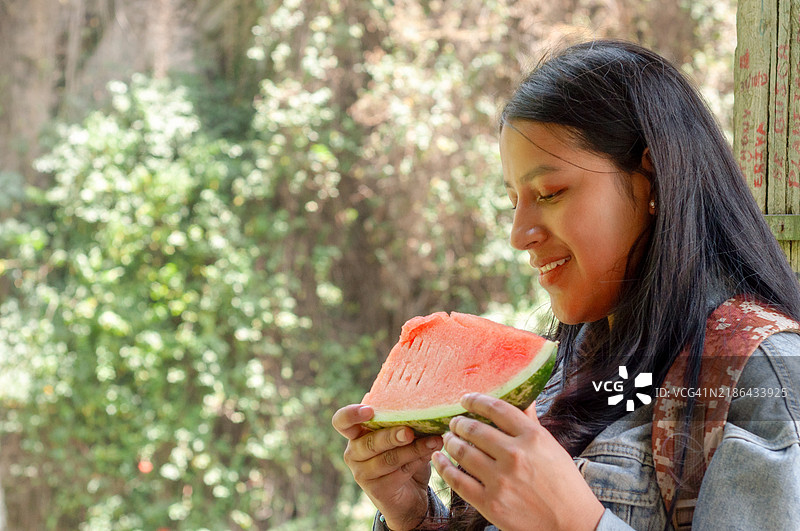 年轻女子背着背包，快乐地吃着一片西瓜，正在热带森林中进行生态旅游探险。图片素材