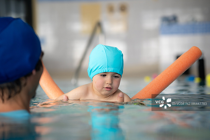 可爱的小男孩在室内游泳池里跟教练学习游泳图片素材
