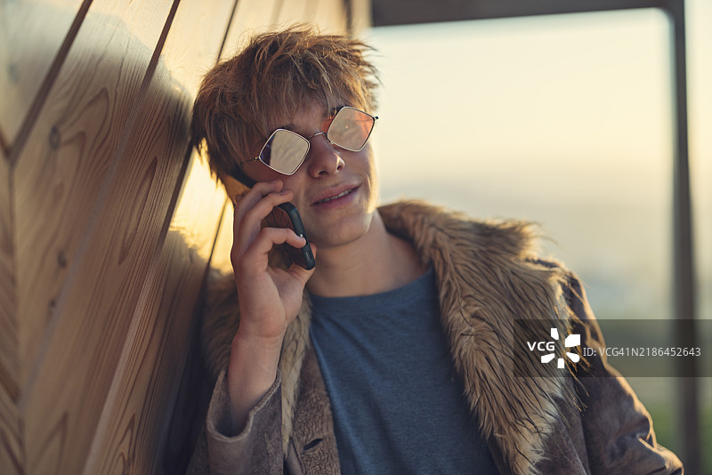 穿着假毛皮外套的青少年靠在木墙上打电话的肖像图片素材