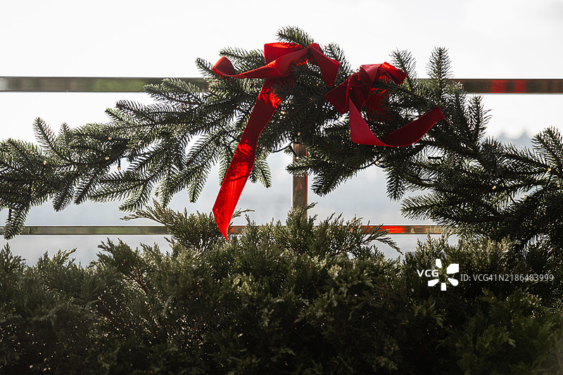 新年装饰的枝条，缠绕着丝带和花环，靠在模糊的城市天际线栏杆上。图片素材