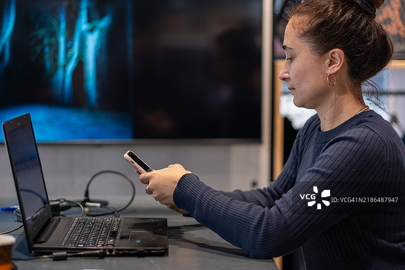 女性在现代办公室使用智能手机和笔记本电脑图片素材