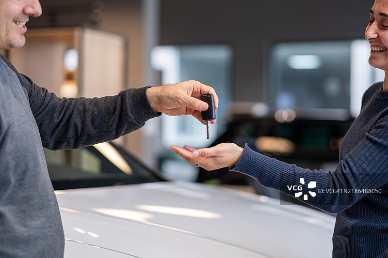 汽车销售员在汽车经销商处将钥匙递给一位女性图片素材