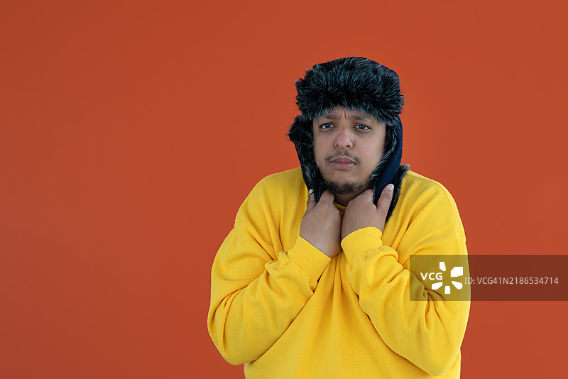 一个人在橙色背景下穿着乌什anka帽子，感到寒冷。图片素材