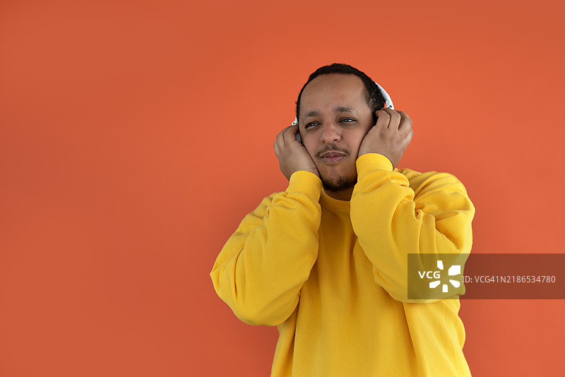 一个戴着耳机的人在纯色背景下聆听音乐，享受这一体验。图片素材