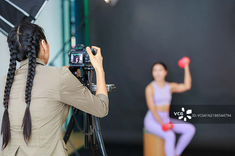 专业女性摄影师在摄影棚拍摄模特：这张图片展示了一位女性摄影师在现代摄影棚中工作，熟练地指导一场与时尚模特的拍摄。图片素材
