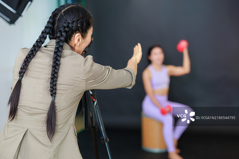 专业女性摄影师在摄影棚拍摄模特：这张图片展示了一位女性摄影师在现代摄影棚中工作，熟练地指导一场时尚模特的拍摄。图片素材