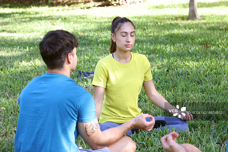 两个拉丁裔千禧一代朋友穿着运动服在公园一起冥想。图片素材