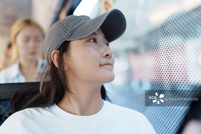 女人在阳光明媚的日子里，若有所思地望着公交车窗外。图片素材