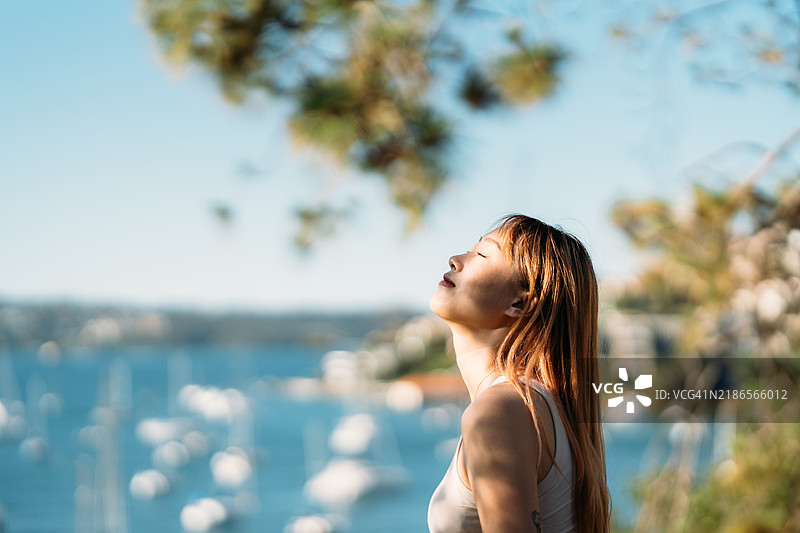 女人在阳光下沐浴，享受宁静的水边景色图片素材
