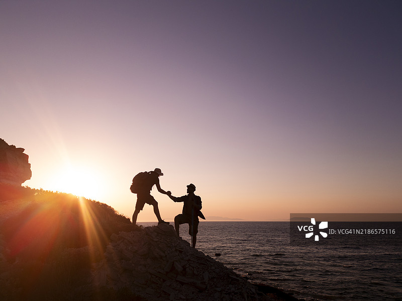 登山者在日落时互相帮助攀爬岩石图片素材