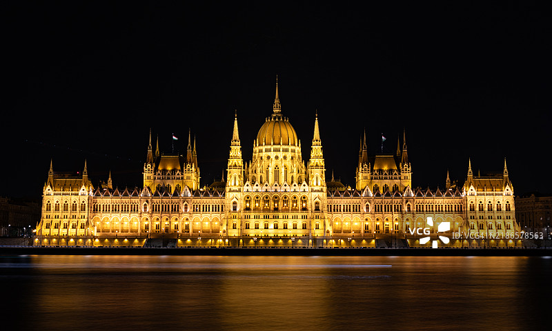 匈牙利国会大厦的外观在夜晚的多瑙河上闪耀，霓虹灯照亮的游船穿梭其间。图片素材