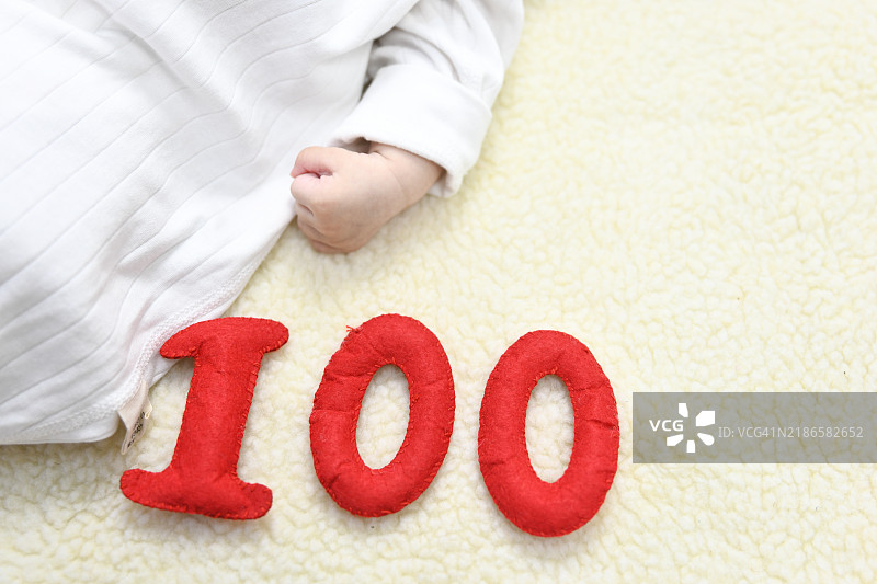 新生儿的100天照片背景。婴儿女孩的手，毯子上有数字100。平面设计概念。图片素材