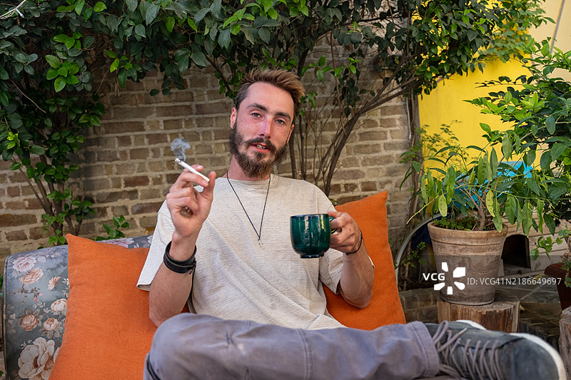 年轻男子在花园里抽烟喝咖啡图片素材