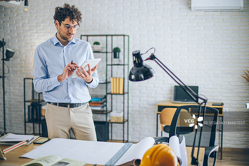 现代建筑师在明亮的现代办公室中使用平板电脑，桌上放着蓝图图片素材
