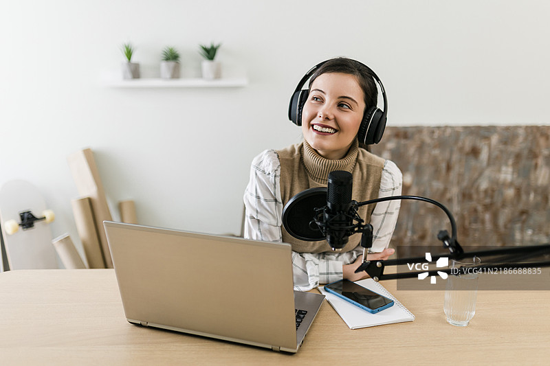 年轻的微笑女性在录音室使用麦克风和耳机录制播客和进行直播图片素材