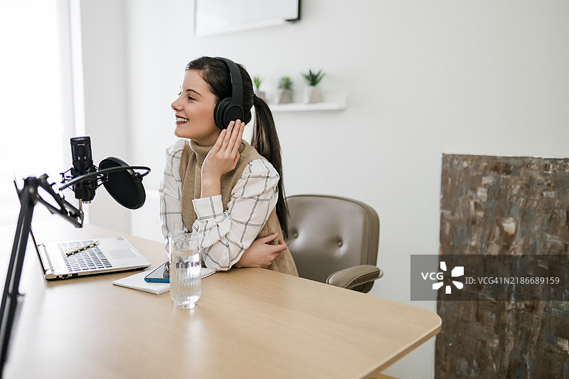 年轻的微笑女性在录音室使用麦克风和耳机录制播客和进行直播图片素材
