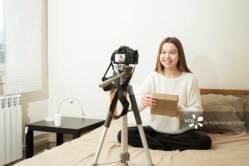 一位年轻的白人女性博主在镜头前录制开箱产品的视频。图片素材