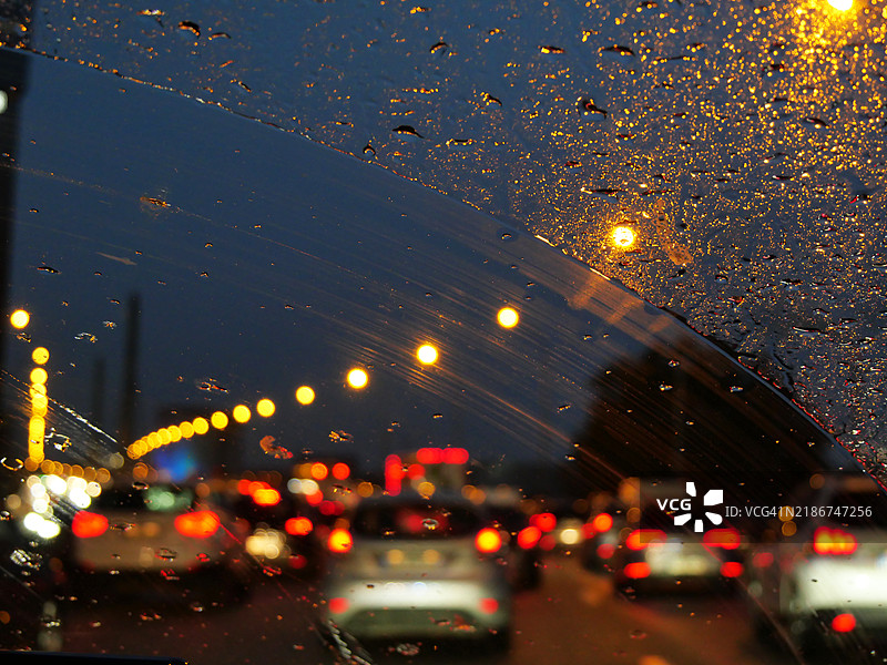模糊的夜间照片，通过雨水浸湿的挡风玻璃拍摄，显示了在法国巴黎道路上堵车的汽车。自然色彩。图片素材