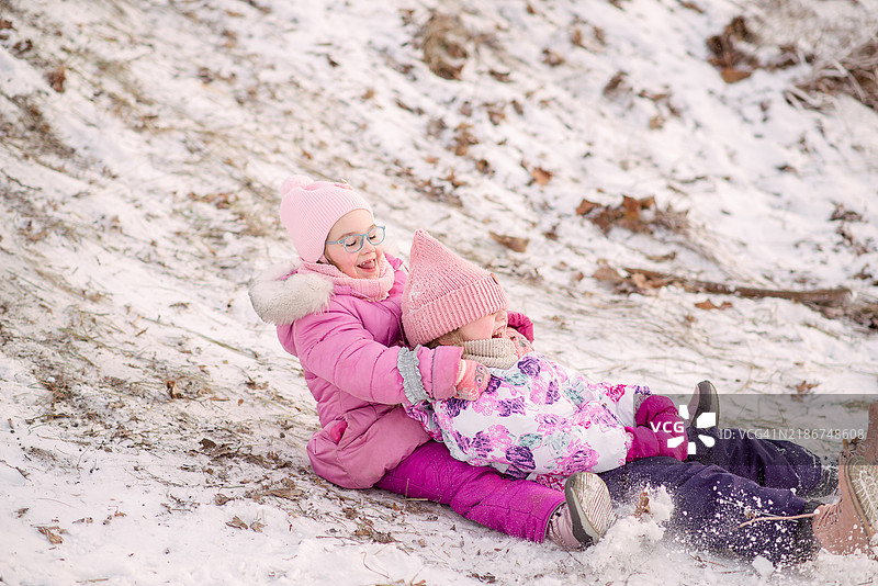 两个女孩朋友在冬天玩雪上游戏，滑雪橇下坡，享受冬季乐趣图片素材