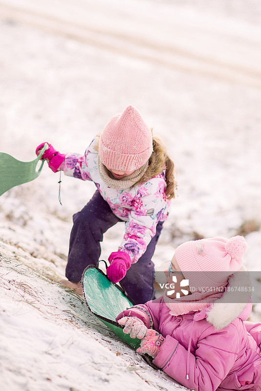 两个女孩朋友在冬天玩雪上游戏，滑雪橇下坡，享受冬季乐趣图片素材