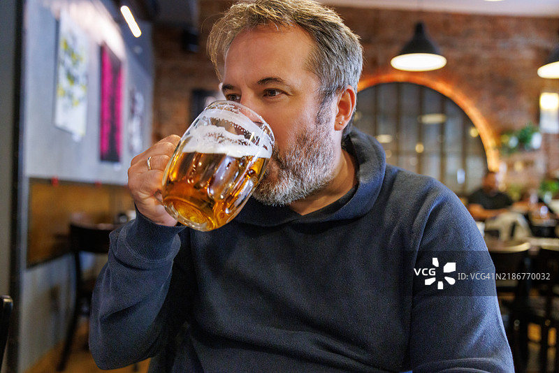 中年男子坐在高档餐厅里，喝着大杯拉格啤酒。图片素材