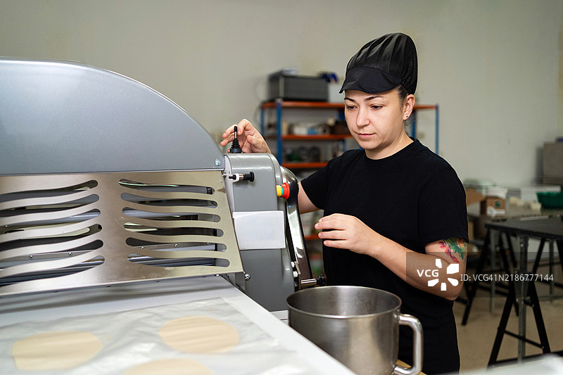 女性面包师在面包店使用面团压延机，准备烘焙面团图片素材