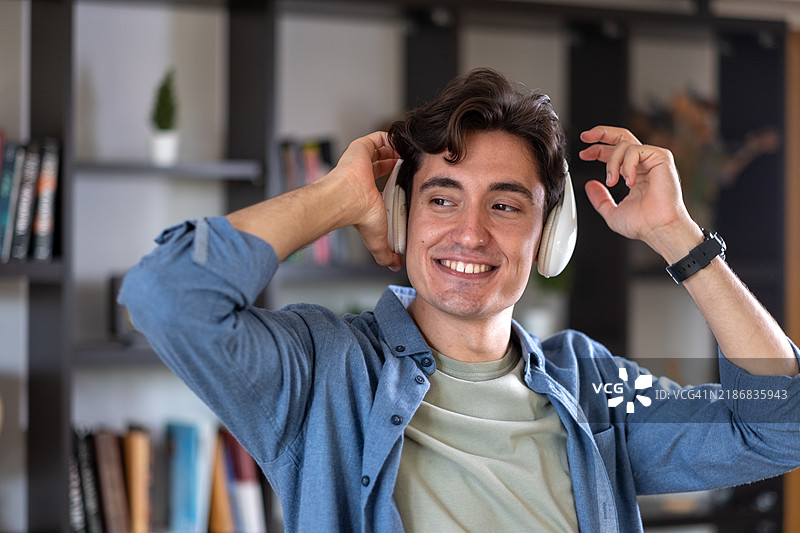 年轻男子在家中享受音乐，戴着耳机图片素材
