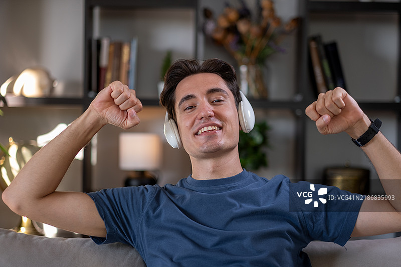 年轻男子坐在沙发上享受音乐，佩戴无线耳机图片素材