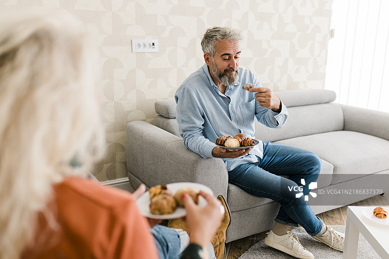 成熟夫妇在家沙发上边吃饼干边交谈放松。图片素材