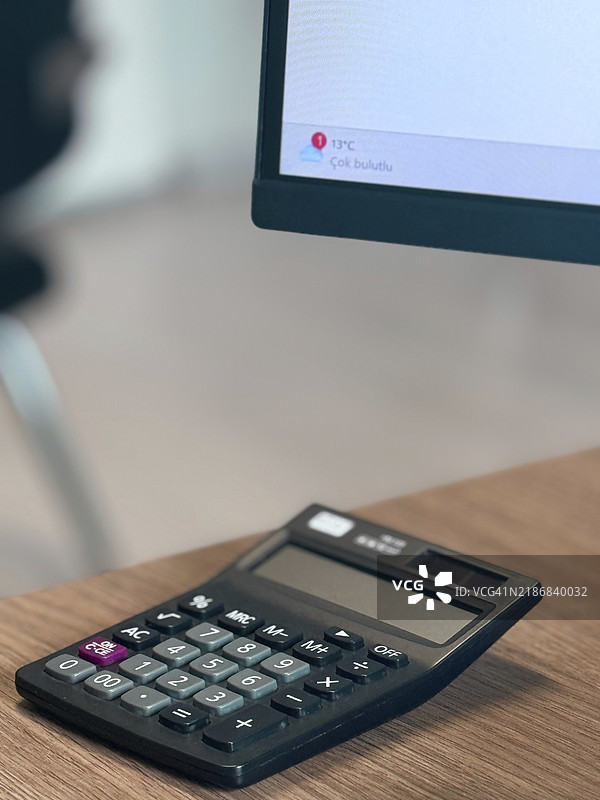 办公环境中，桌子上放着一台黑色计算器，旁边有一台电脑显示器。图片素材