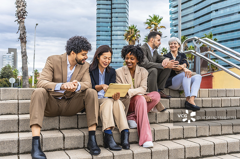 多元种族和多样化的商业人士坐在户外台阶上使用平板电脑工作图片素材