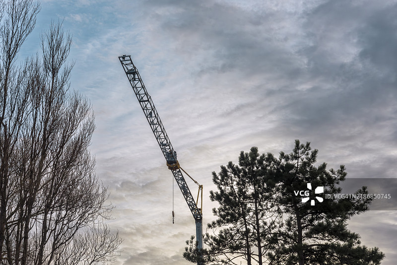 工业起重机两侧有树木，突显在多云的天空下。图片素材
