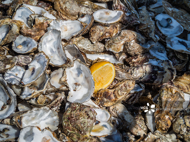 堆放着开口和闭合的生蚝，旁边有一个柠檬，拍摄于康卡尔，这是街头食品摊位的剩余物，位于伊勒-维莱讷 - 布列塔尼（布列塔尼） - 法国西部。康卡尔的生蚝养殖被列入联合国教科文组织非物质文化遗产。图片素材