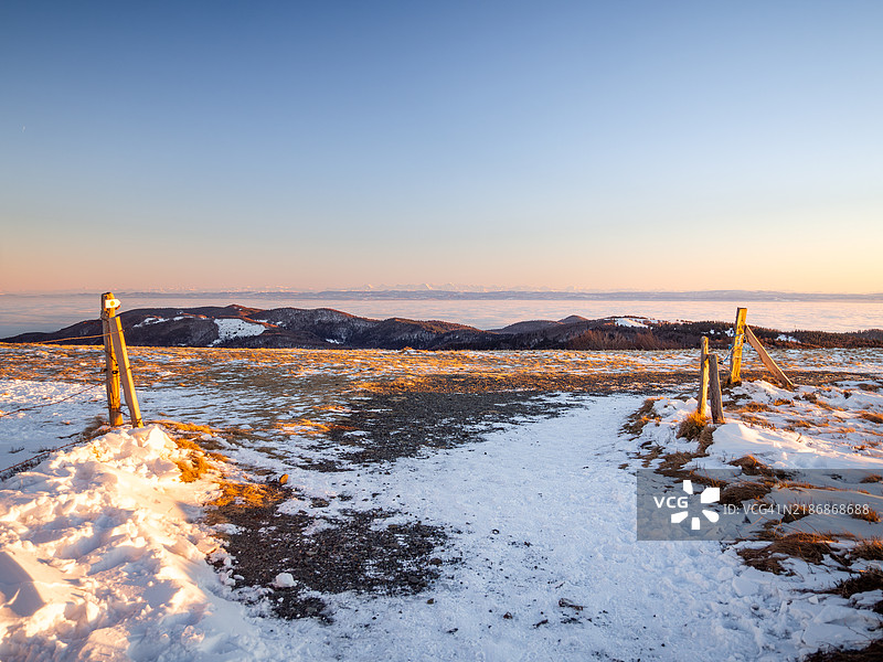 冬季日落时分,阿尔萨斯的巴隆达尔萨峰顶雪-covered徒步小径的景色,远处是沃日山脉和瑞士阿尔卑斯山,之间是一片雾海,阿尔萨斯 - 大东部 - 法国东部。图片素材
