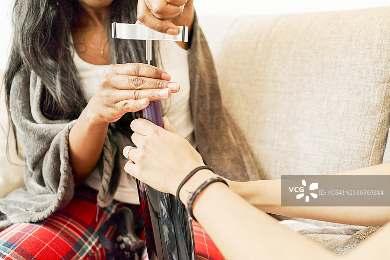 女人的手从沙发上的一瓶葡萄酒中拔出软木塞的正面视图图片素材