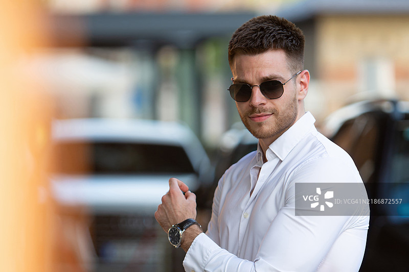 年轻商人在现代商务办公楼外穿着白衬衫和黑色太阳镜图片素材
