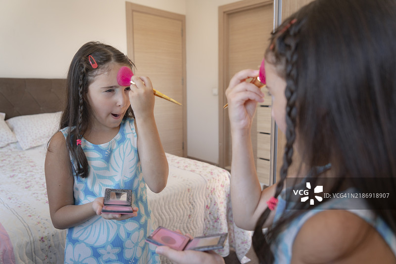 可爱的小女孩在镜子前化妆并看着自己的倒影图片素材