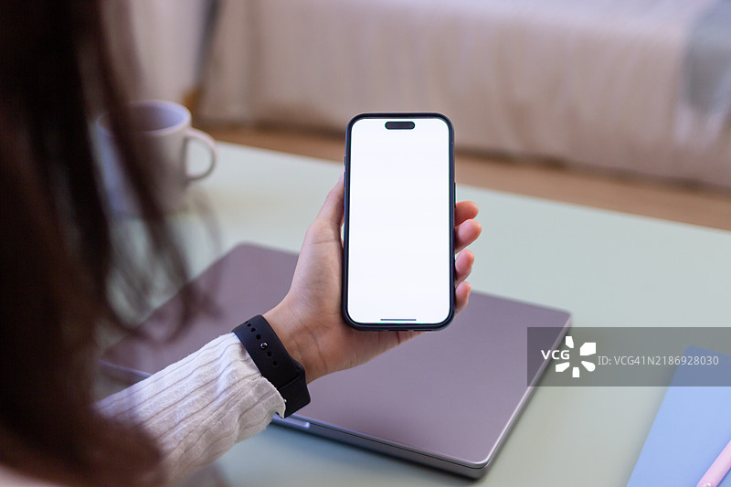 女性在家办公时手持一部空白屏幕的智能手机图片素材