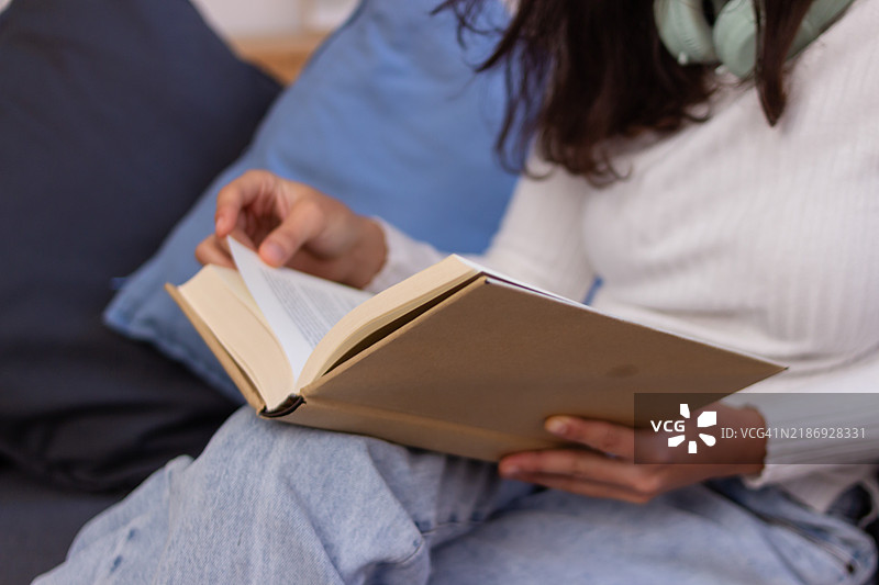 年轻女性在家里的沙发上阅读一本书图片素材