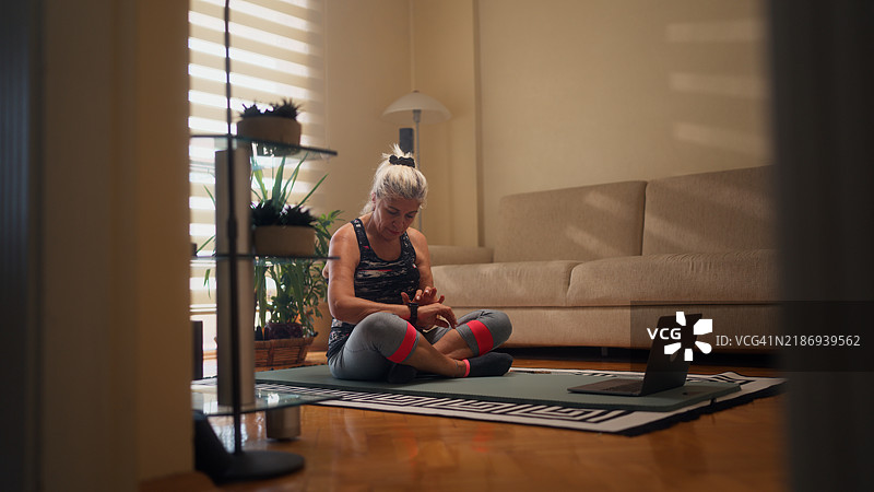积极的老年女性运动员在家中开始锻炼前设置她的智能手表图片素材