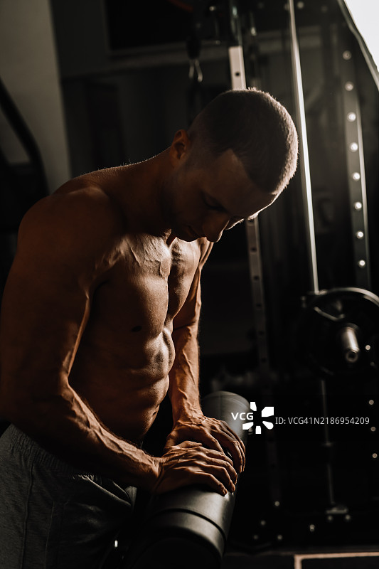 健身房里，健壮的男性教练在无上衣的情况下展示手臂的肌肉线条。图片素材