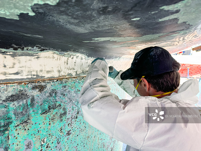 男子用刮刀从帆船的龙骨和船体上去除防污漆图片素材