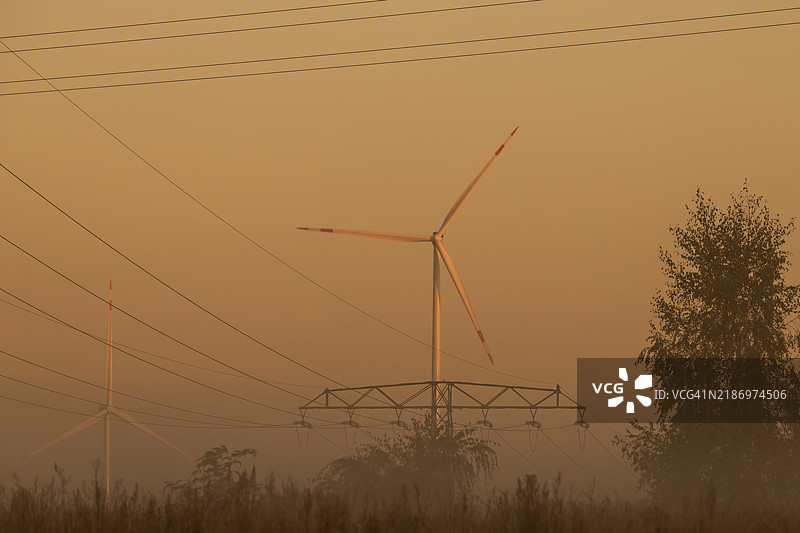 雾霭笼罩的清晨，电力塔与风力涡轮机在日出时分的景象图片素材