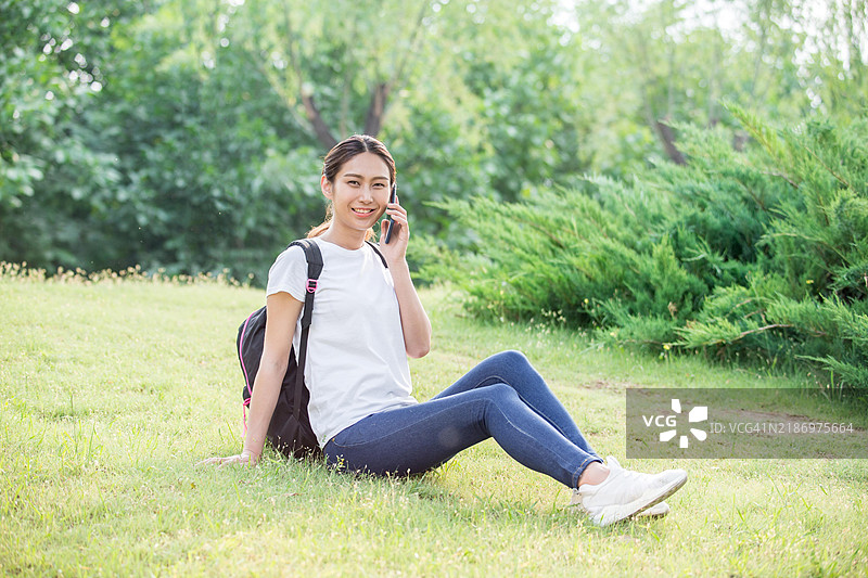一位年轻女性坐在草地上打电话。图片素材